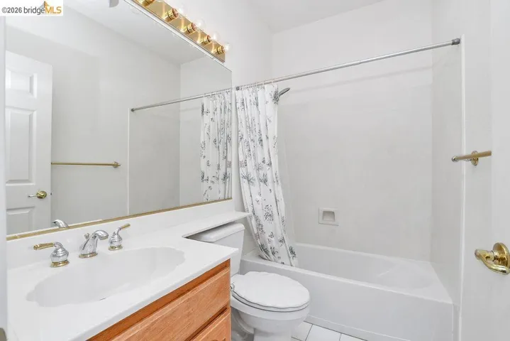 Bathroom featuring a single vanity with an integrated sink, polished brass and chrome fixtures, a full-width mirror, and a combination bathtub/shower with white surround