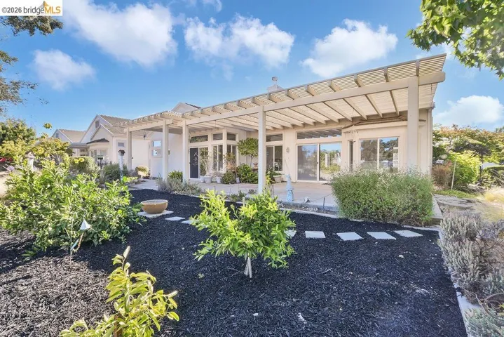 Rear exterior featuring an extensive patio with a slatted pergola, multiple large sliding glass doors, and manicured landscaping with stepping stones