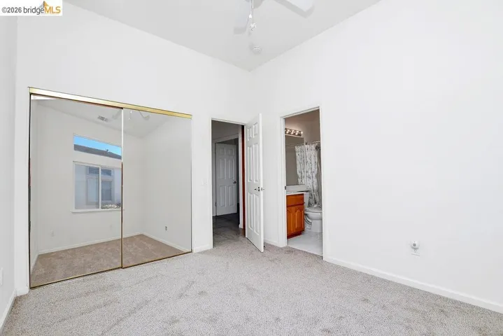 Carpeted interior space featuring mirrored sliding closet doors, a vaulted ceiling, and an en-suite bathroom with a wood-finish vanity
