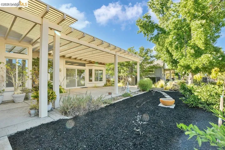 Expansive patio area featuring a white slatted pergola and concrete surface