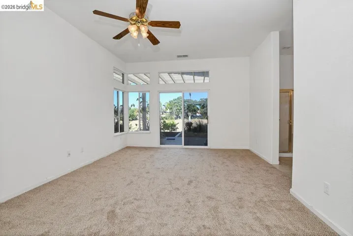 Spacious room featuring vaulted ceilings, a ceiling fan with integrated lighting, and neutral carpet flooring