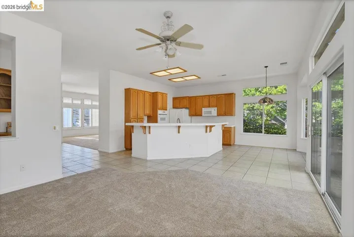 Spacious interior featuring a kitchen with wood cabinetry, white appliances, an island with seating, and tile flooring