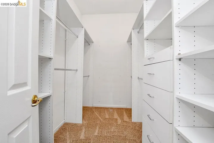 White custom closet system featuring adjustable shelving, multiple hanging rods, built-in drawers with brushed nickel hardware, and beige carpet flooring