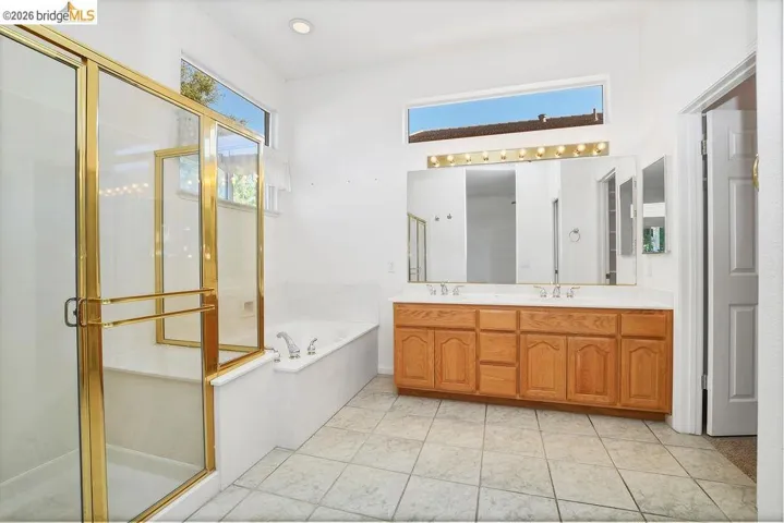 Bathroom featuring a glass-enclosed shower with brass-finish framing, a separate built-in bathtub, and a dual-sink vanity with light wood cabinetry
