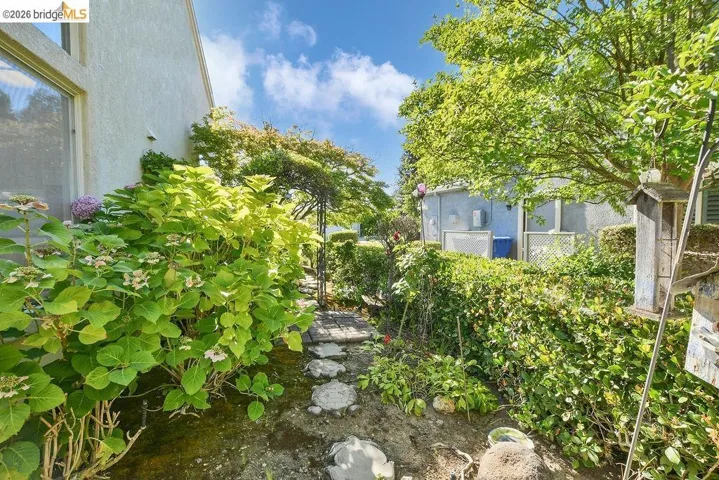 Landscaped side yard featuring stepping stones, mature shrubs, and a metal arbor