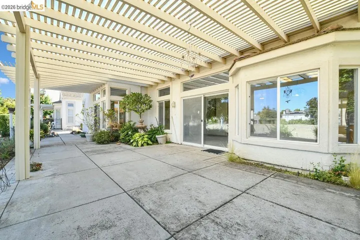 Expansive concrete patio featuring a louvered pergola covering, a sliding glass door entry, and multiple large windows