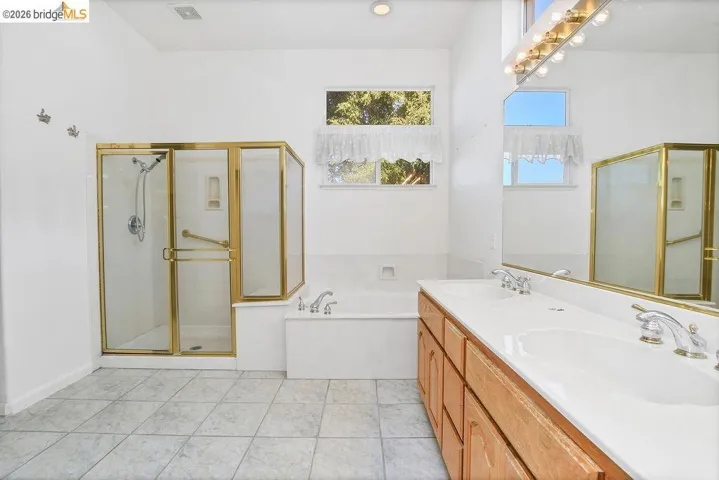 Bathroom featuring a dual vanity with integrated sinks, a built-in tub, and a separate glass-enclosed shower with a gold-tone frame