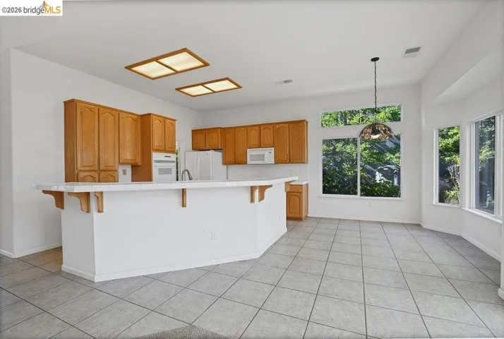 Open-concept kitchen featuring light wood cabinetry, white tile countertops, and a peninsula island