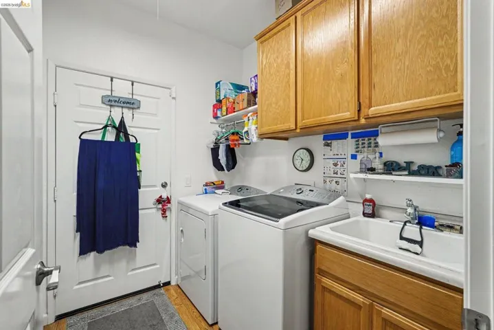 Dedicated laundry room featuring wood-finish flooring, a utility sink with base cabinetry, and overhead storage cabinets