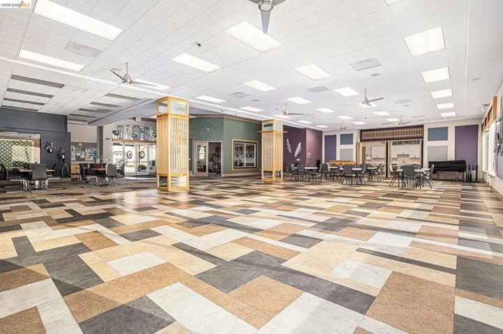 Spacious interior featuring geometric pattern flooring, a grid ceiling with integrated lighting, and multiple ceiling fans