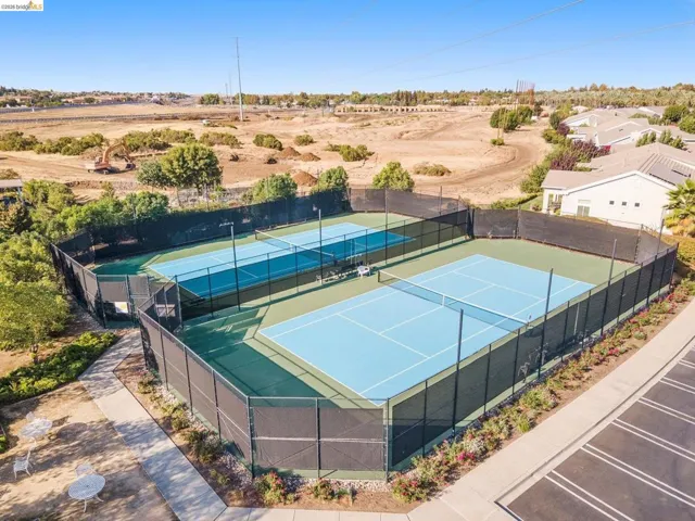 Two tennis courts with blue playing surfaces and green surrounds, enclosed by black fencing