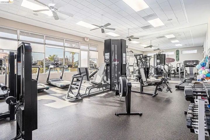 Fitness center featuring rubber flooring, extensive window line, ceiling-mounted fans, recessed lighting, and full-wall mirrors