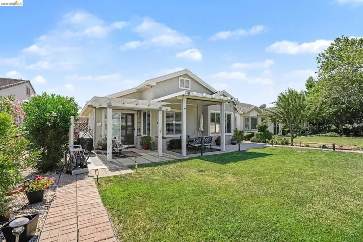Rear exterior of a single-story residence featuring a large grassy lawn and mature landscaping