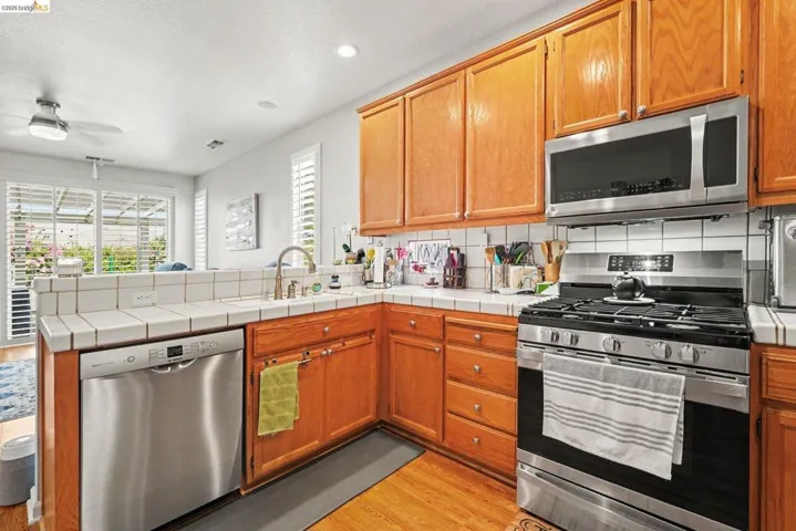 Expanded kitchen featuring wood cabinetry, stainless steel appliances, tile countertops, and a tile backsplash