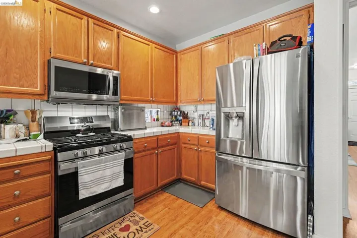Kitchen featuring wood-finish flooring, wood cabinetry, stainless steel appliances, tile countertops, and a white subway tile backsplash