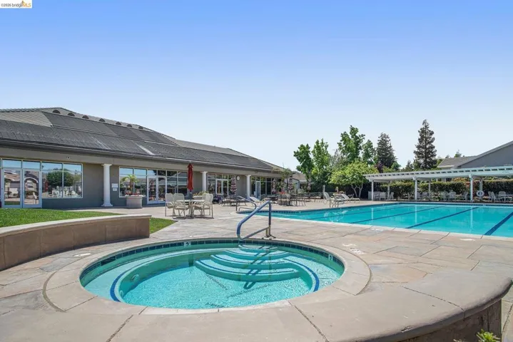 Community pool area featuring a large swimming pool, integrated spa, and surrounding patio space with a pergola