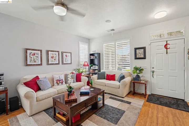 Living area with wood-finish flooring, white plantation shutters, and a ceiling fan with integrated lighting