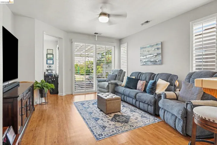 Bright living area featuring wood-finish flooring, a ceiling fan, and white walls