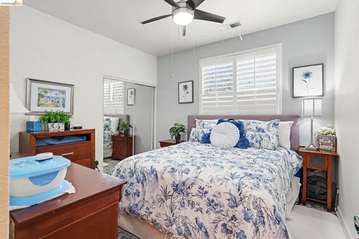 Bedroom featuring a ceiling fan with integrated lighting, window with white plantation shutters, and a sliding mirrored closet door