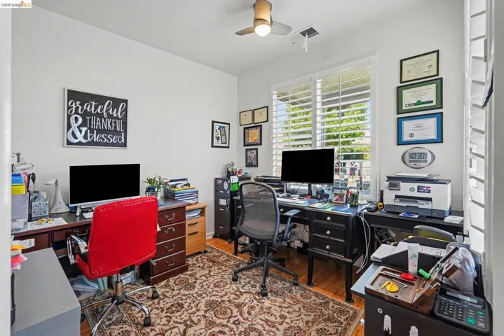 Dedicated office space featuring two workstations, a ceiling fan, and window with plantation shutters