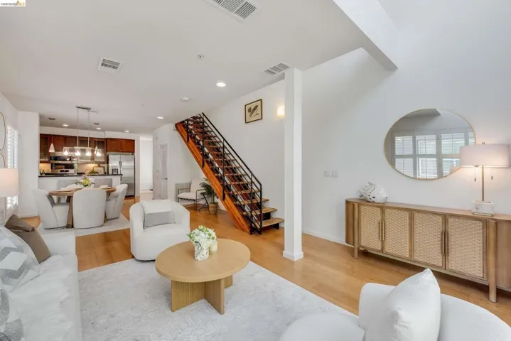 Open-concept living space featuring wood-finish flooring, a modern open-tread staircase with black railing, recessed lighting, and a kitchen with dark wood cabinetry and stainless steel appliances