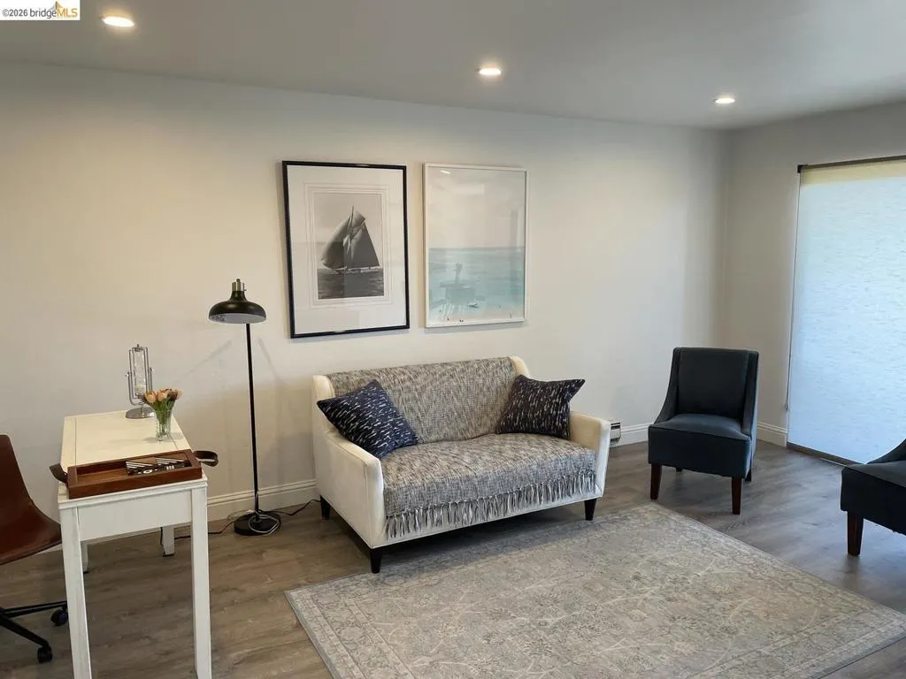 Brightly lit room featuring recessed ceiling lighting, light gray walls, wood-finish flooring, and a large window with privacy shades