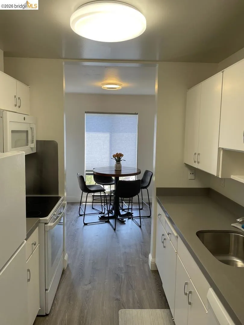 Galley kitchen featuring white cabinetry, gray countertops, and wood-finish flooring