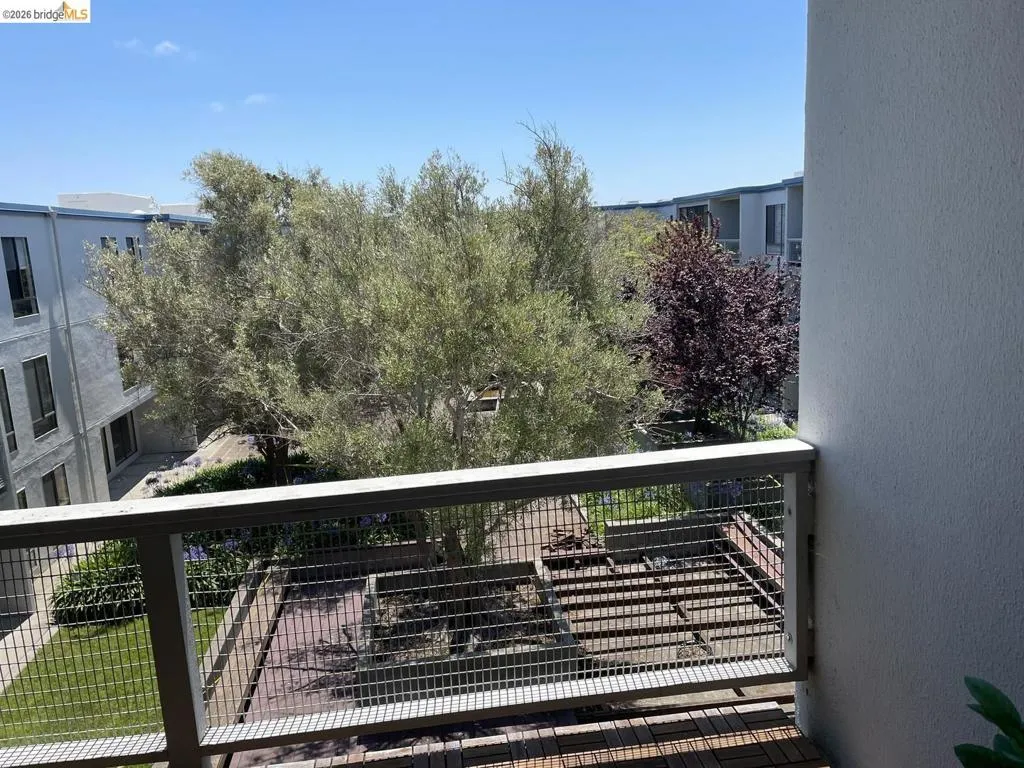Private balcony with slatted wood-finish flooring, metal railing, and a courtyard perspective featuring mature trees and landscaped grounds