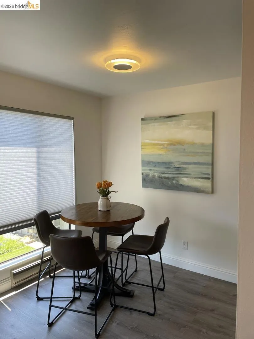 Corner dining area featuring contemporary flooring, a large window with privacy blinds, and a modern flush-mount ceiling light