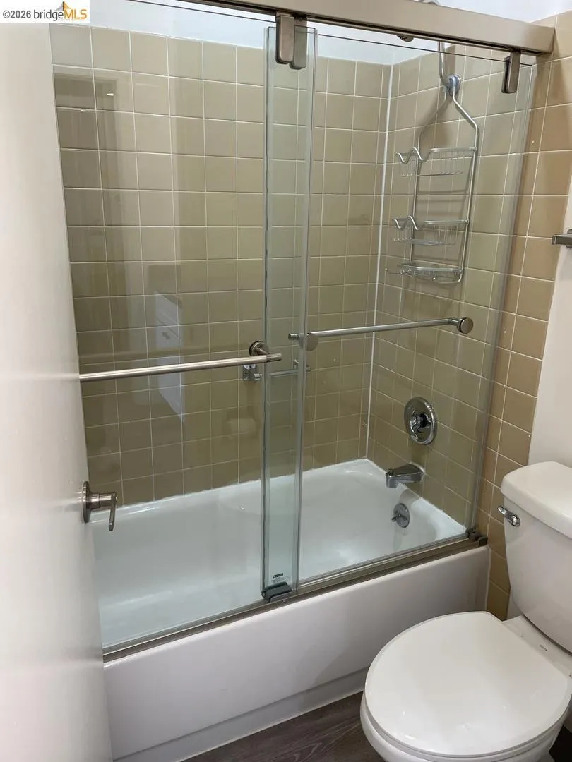 Bathtub with sliding glass shower doors and tan square tile surround