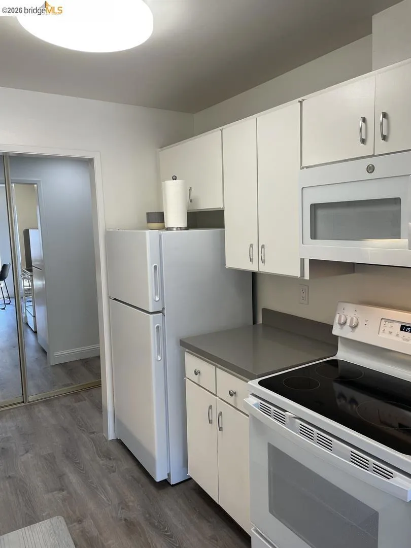 Kitchen featuring white cabinetry, gray countertops, a built-in microwave, white refrigerator, and wood-finish flooring