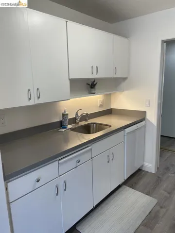 Kitchen featuring white cabinetry with silver hardware, gray countertops, a stainless steel sink with a gooseneck faucet, and wood-finish flooring