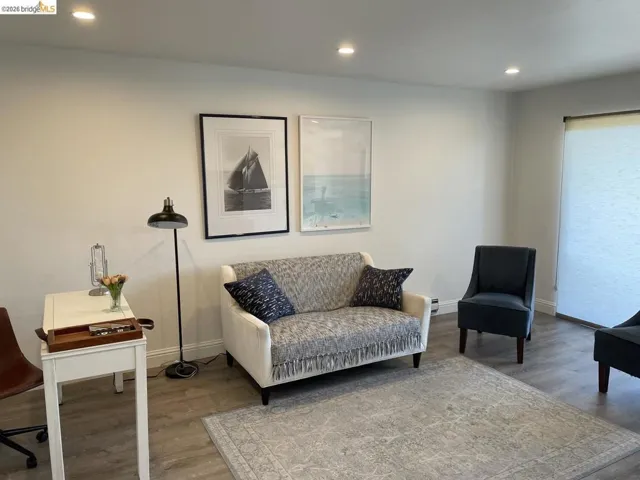 Brightly lit room featuring recessed ceiling lighting, light gray walls, wood-finish flooring, and a large window with privacy shades