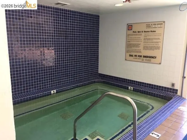 Indoor spa with blue mosaic tile surround, white wall tile, and a stainless steel grab rail