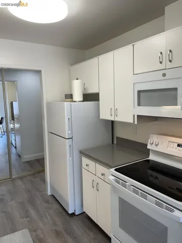 Kitchen featuring white cabinetry, gray countertops, a built-in microwave, white refrigerator, and wood-finish flooring
