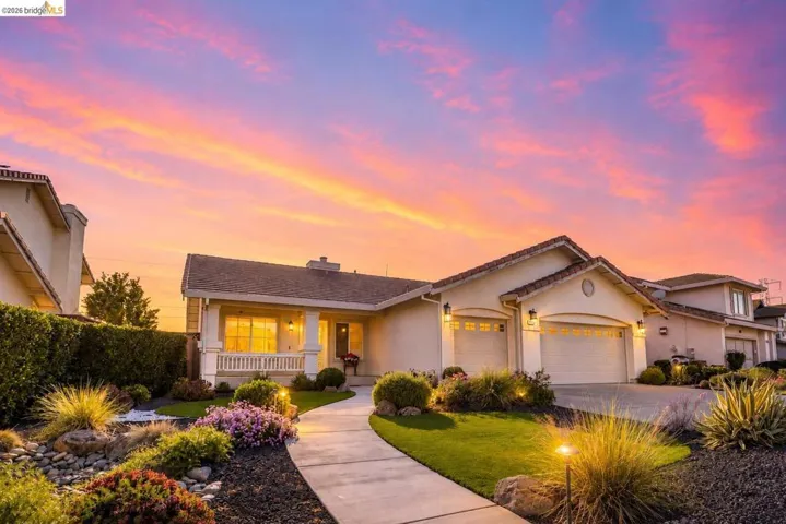 Stucco exterior residence with a multi-car garage, front porch featuring white columns and railing, and a winding concrete pathway