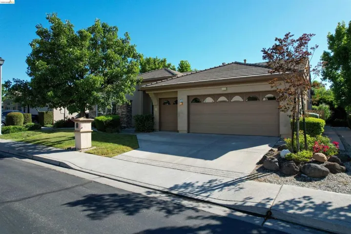 Tan stucco facade with stone accents, a tile roof, and an attached two-car garage