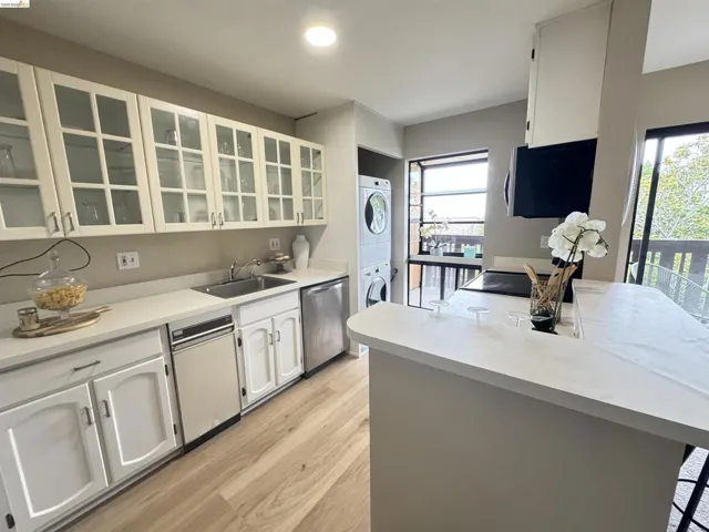 Kitchen featuring light wood-finish flooring, white cabinetry with glass-front upper doors, light-toned countertops, and stainless steel appliances