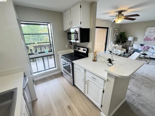 Kitchen featuring white cabinetry, light-toned wood-finish flooring, stainless steel appliances, and a pass-through bar-height counter