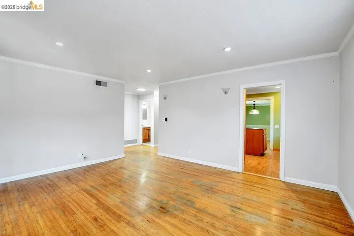Spacious room featuring wood-finish flooring, light grey walls, and white crown molding
