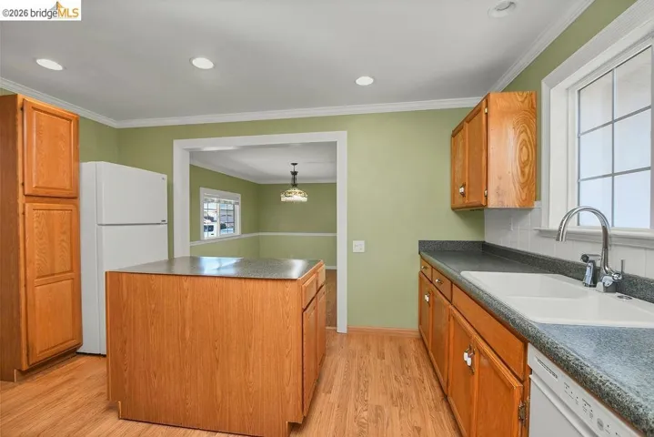 Kitchen featuring wood-finish flooring, an integrated island, light wood cabinetry, recessed ceiling lighting, and a window with grid detailing
