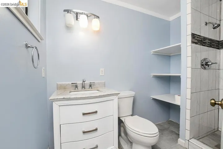 Bathroom featuring a white vanity with a stone countertop, a shower with tiled walls and a decorative accent band, and built-in shelving