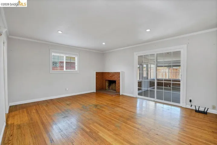 Bright interior with wood-finish flooring, a brick fireplace, a window with horizontal blinds, and sliding glass doors featuring multiple panes