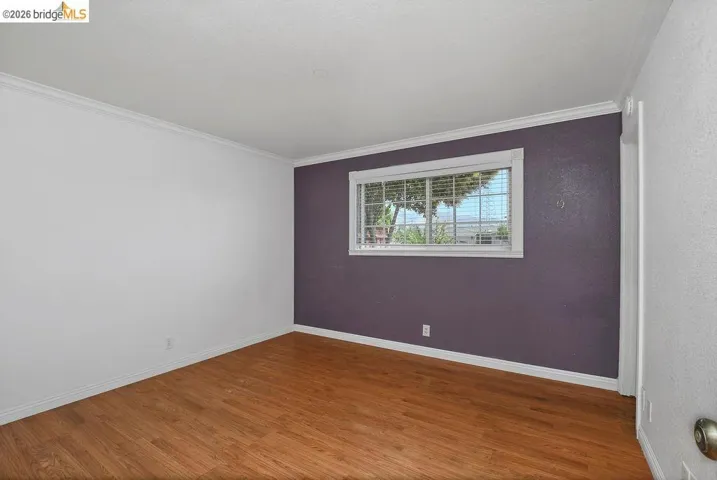 Interior room featuring wood-finish flooring, white baseboards, and crown molding