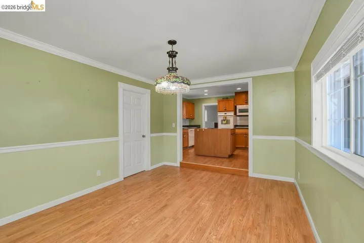 Spacious room featuring wood-finish flooring, light green walls with white chair rail molding, and a decorative ceiling light fixture