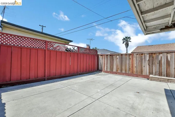 Concrete patio area featuring a red lattice-top privacy fence and natural wood fencing