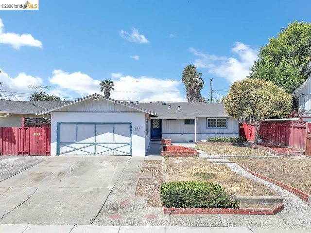 Single-story residence featuring an attached garage with a decorative door, a driveway, and a front yard with brick-lined planters