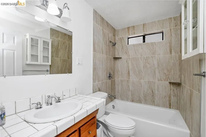 Bathroom featuring a tiled shower surround, recessed window, white bathtub, and vanity with an integrated sink and tiled countertop