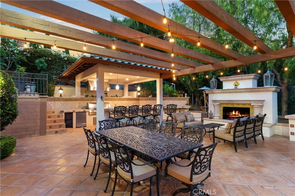 Expansive outdoor entertaining space featuring a fireplace, built-in BBQ, bar seating, and multiple gathering areas.