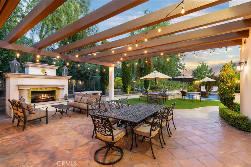 Expansive outdoor entertaining space featuring a fireplace, built-in BBQ, bar seating, and multiple gathering areas.